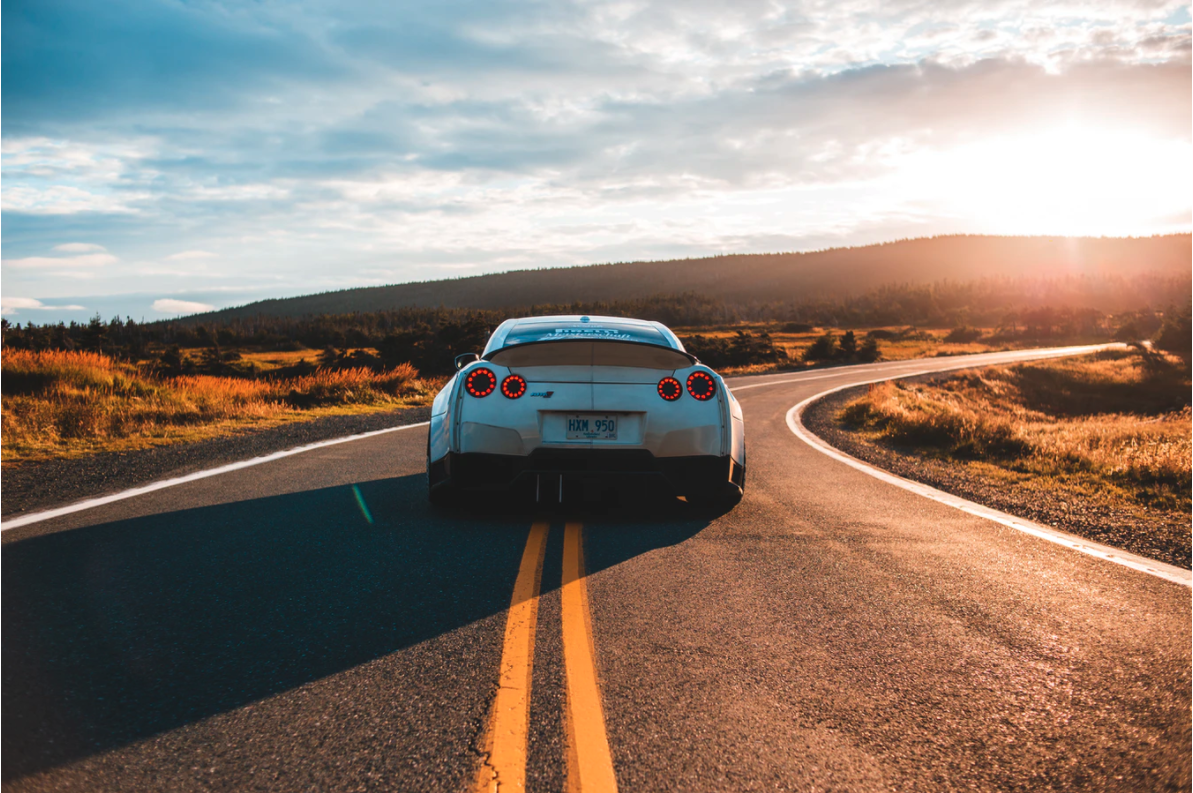 A white sports car driving on a sunlit road.