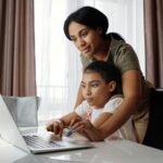 mother helping her daughter use a laptop