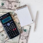 calculator and notepad placed over stack of usa dollars