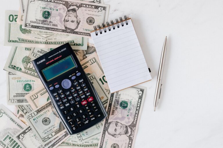 calculator and notepad placed over stack of usa dollars