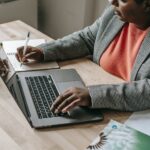 black woman typing on laptop and writing