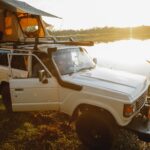 anonymous male traveler sitting in suv car parked near lake at campsite