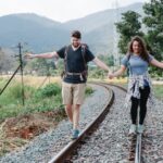 happy couple of hikers holding hands and walking along railroad in countryside