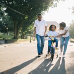 man standing beside his wife teaching their child how to ride bicycle