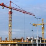 three yellow and red tower cranes under clear blue sky