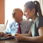 young woman helping senior man with payment on internet using laptop