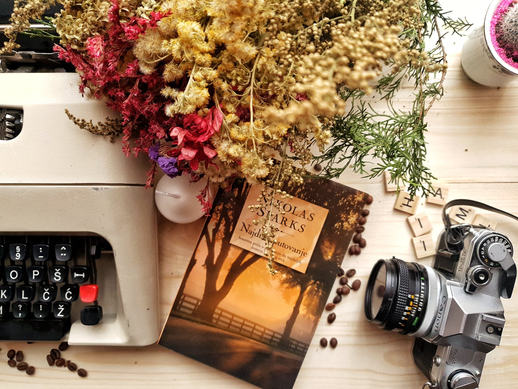 bunch of flowers and book arranged on wooden table with vintage typewriter and camera