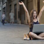 woman raising her hands up while sitting on floor with macbook pro on lap