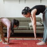 excited barefoot ethnic mother and cute girl doing stretching exercises together