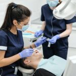 female dentist with assistant curing teeth of patient