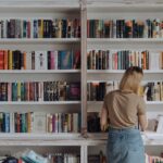 woman in beige shirt and blue denim jeans standing in front of books