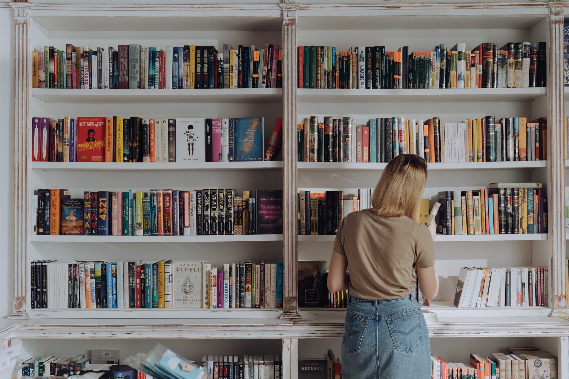 woman in beige shirt and blue denim jeans standing in front of books