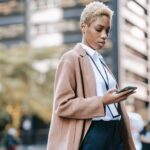 focused black businesswoman browsing smartphone on urban street
