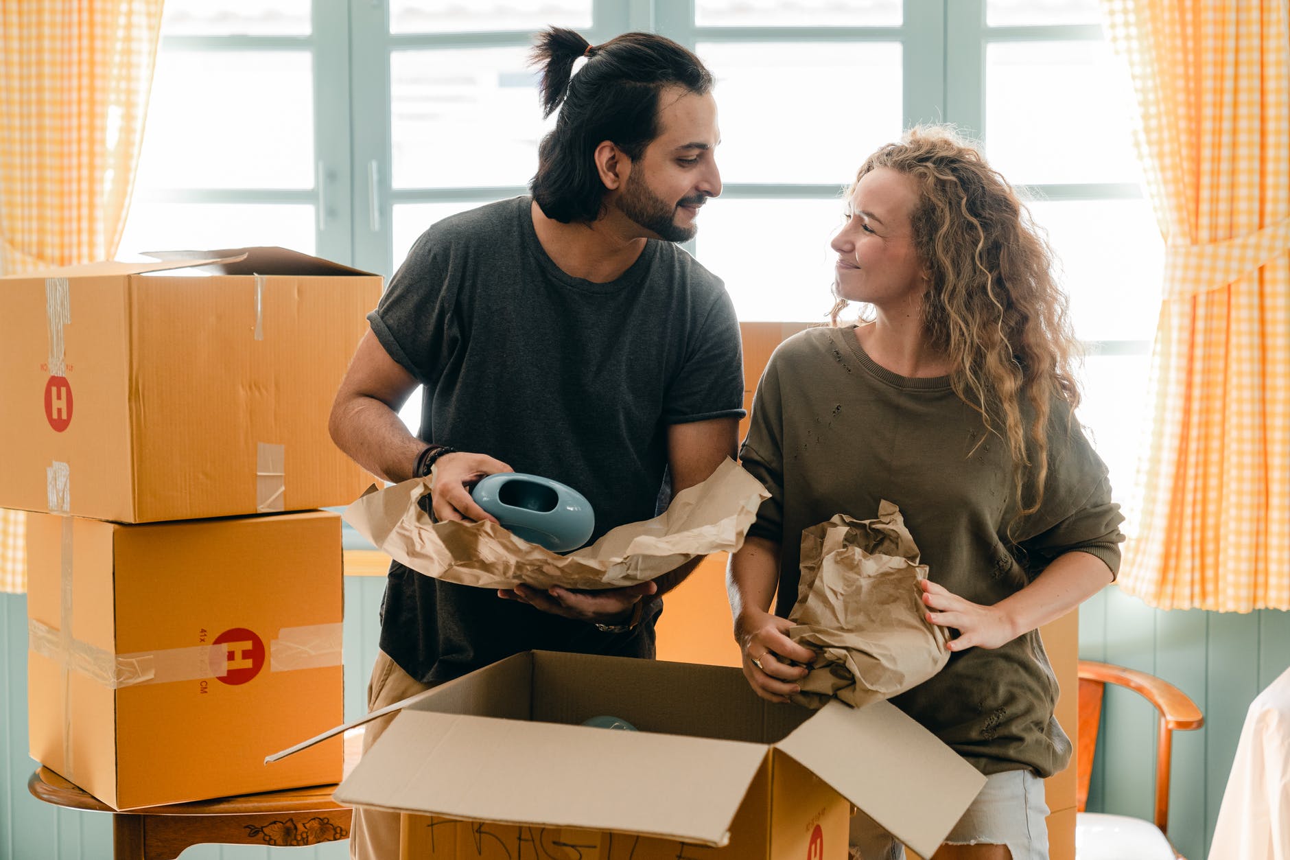 multiethnic couple packing ceramic belongings in parchment before relocation