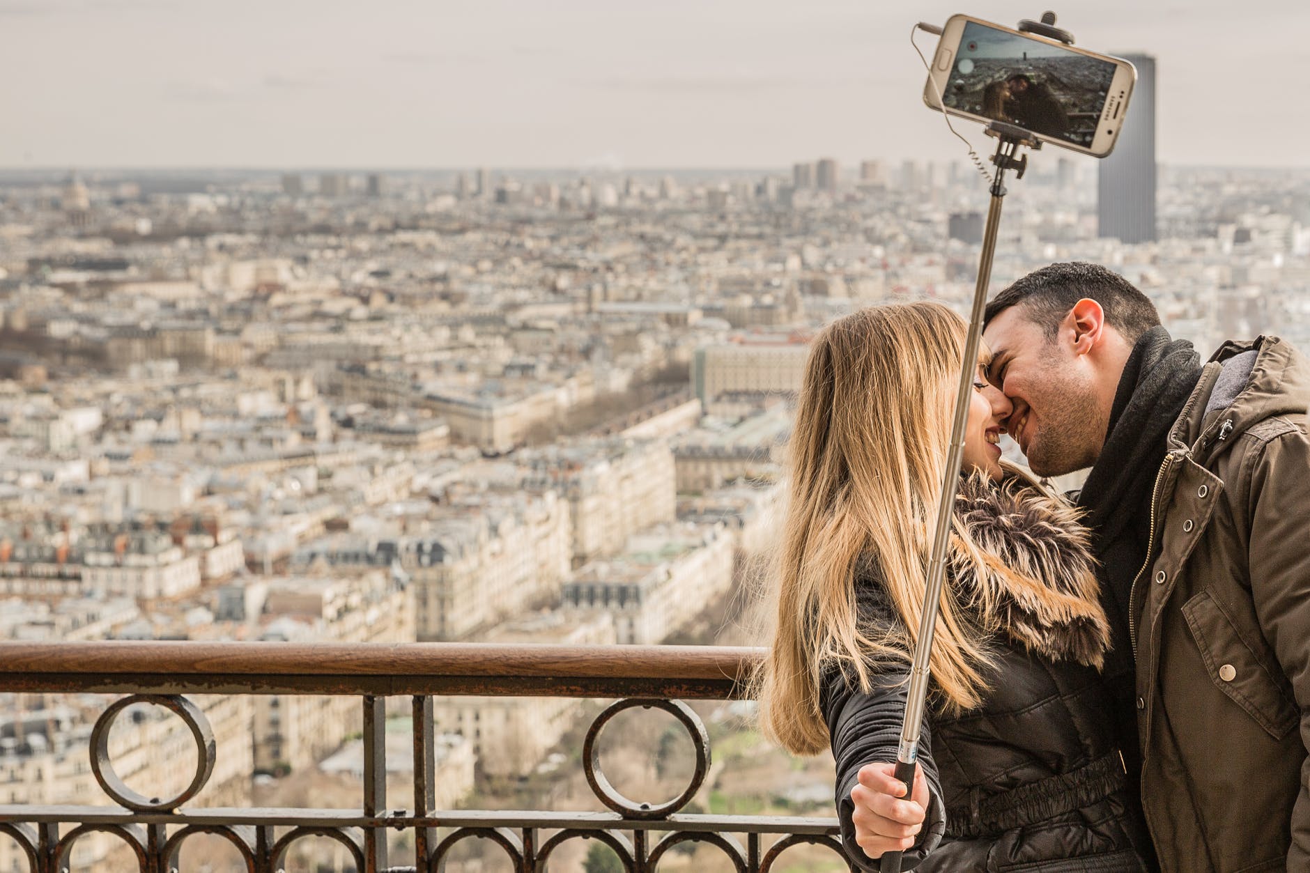 man kissing woman holding selfie stick