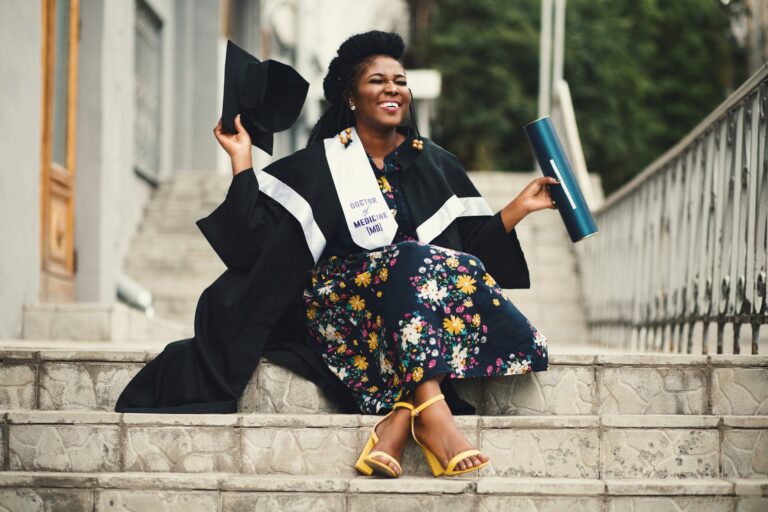 photo of woman wearing academic dress and floral dress sitting on stairway