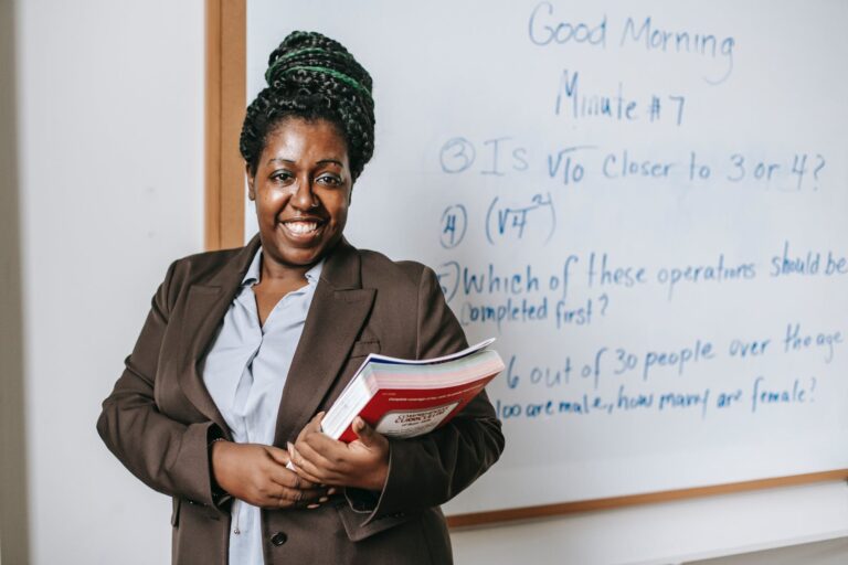 cheerful black female teacher with workbooks standing near whiteboard
