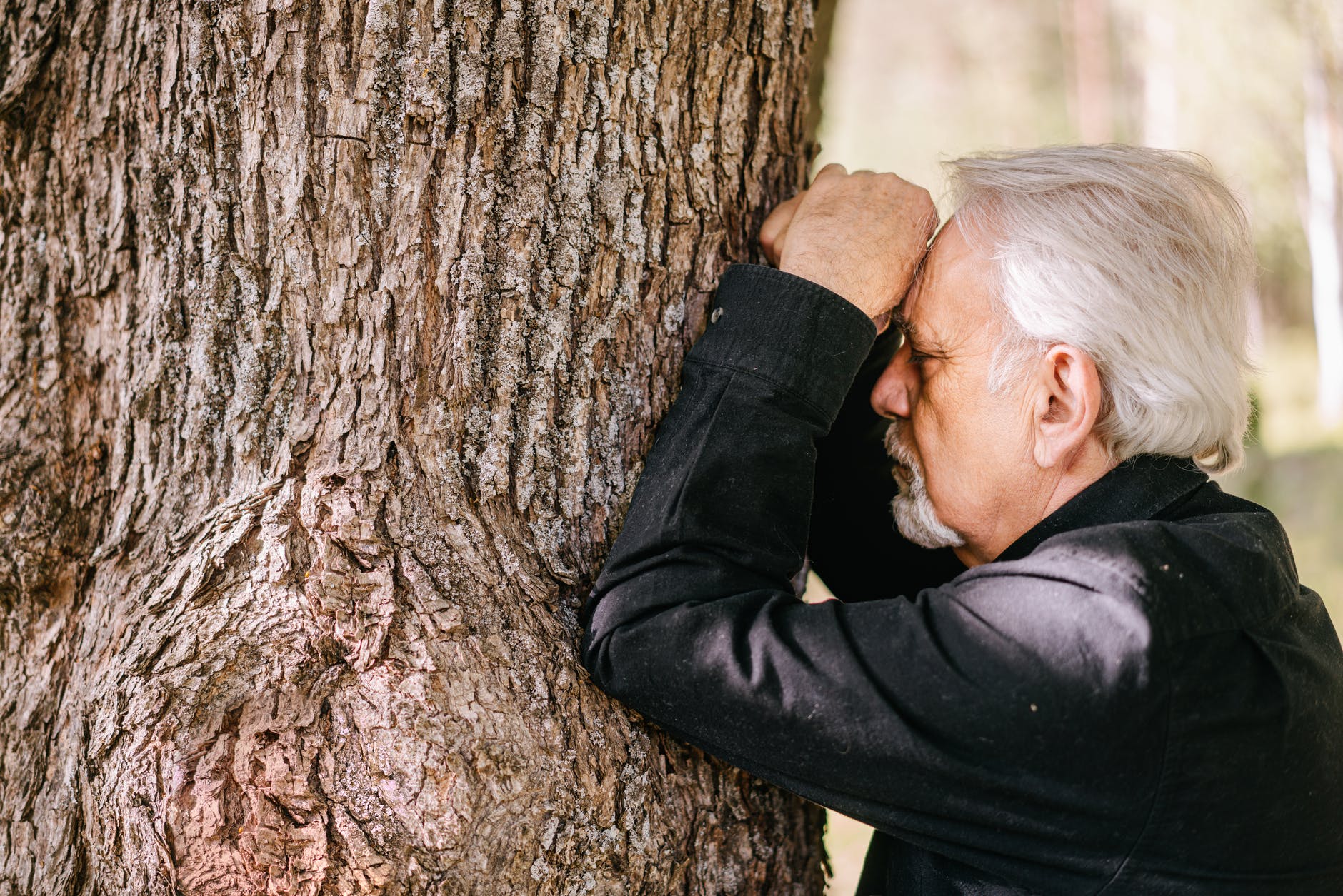 a man in grief leaning on a tree