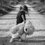 backview of girl holding plush toy while walkingon dirt road