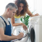 Two people working together to fix a washing machine