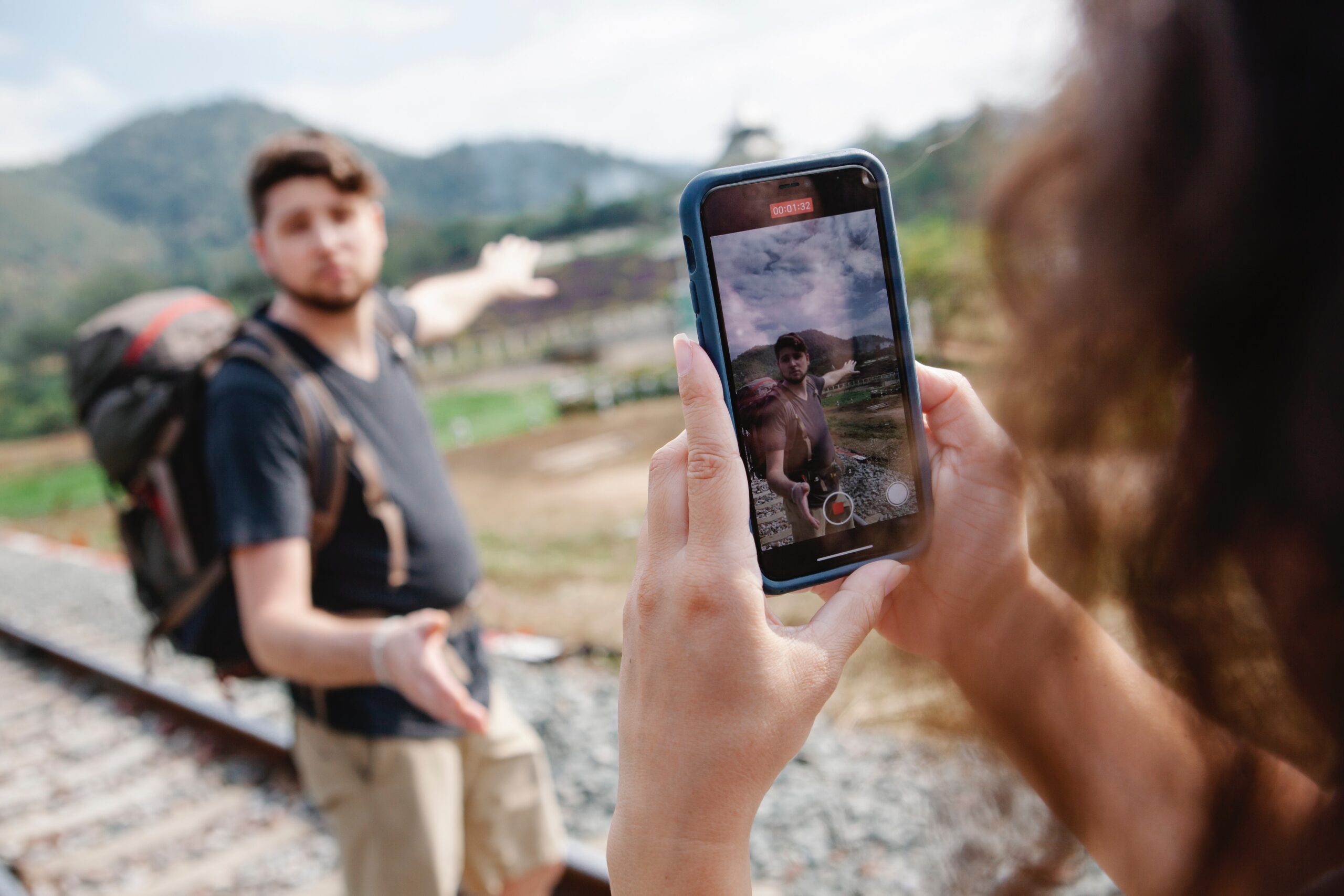 Woman holding phone to take a video of man hiking on a mountain.