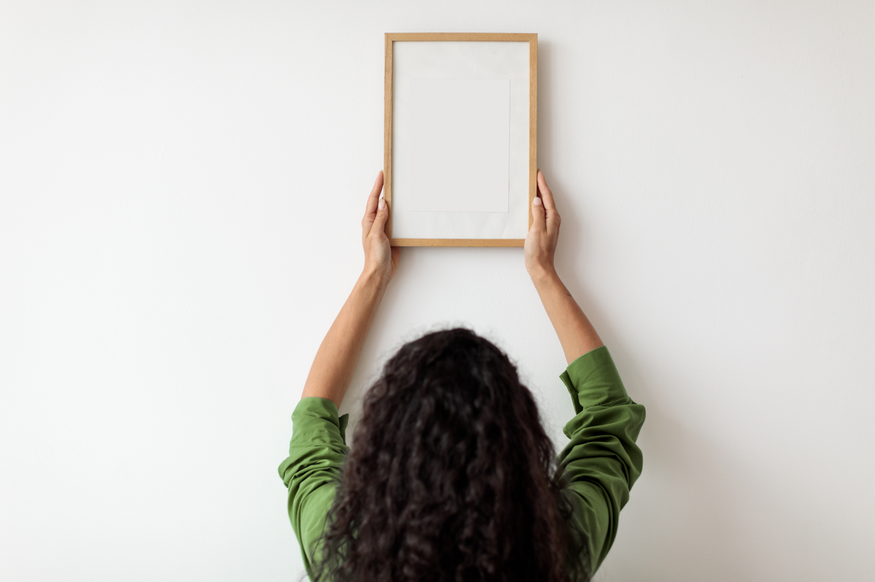 Woman hanging a frame on an otherwise blank wall