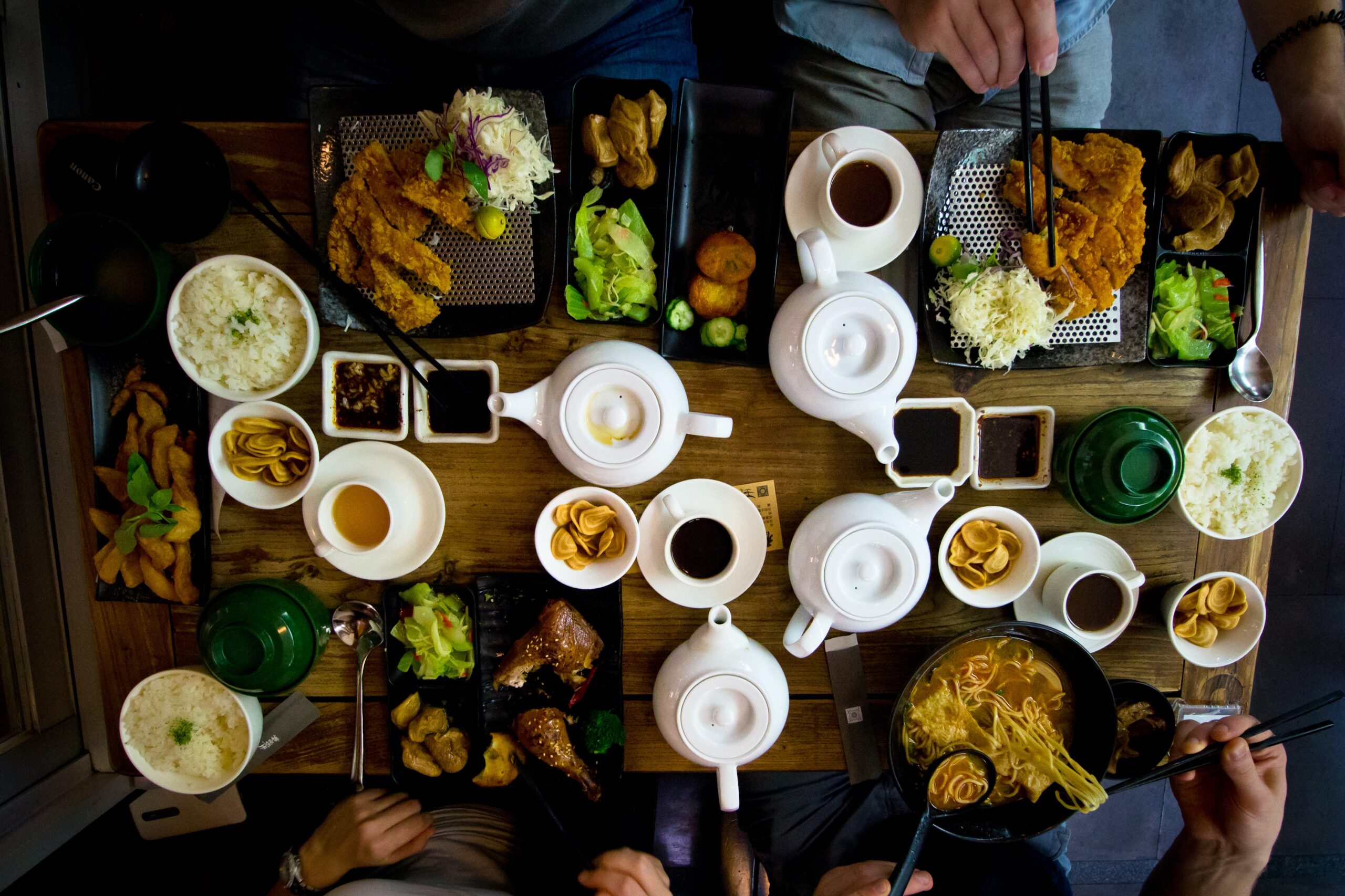 Overhead view of a table filled with plates of food and teapots with people sitting around eating.