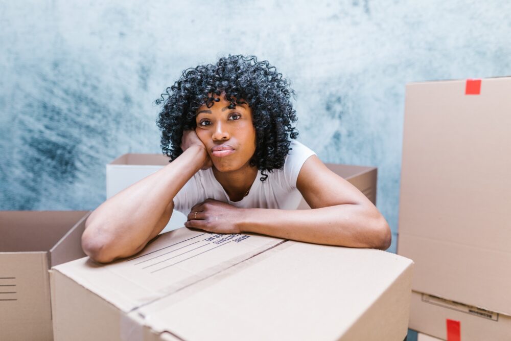 Woman sitting with her arms on top of a packing box with her mouth pouted out.