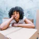 Woman sitting with her arms on top of a packing box with her mouth pouted out.