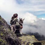 siberian husky beside woman sitting on gray rock mountain hill while watching aerial view