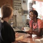 delighted black female barista serving coffee in cup in cafe