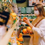 Woman standing in grocery store with a mask on holding an orange.