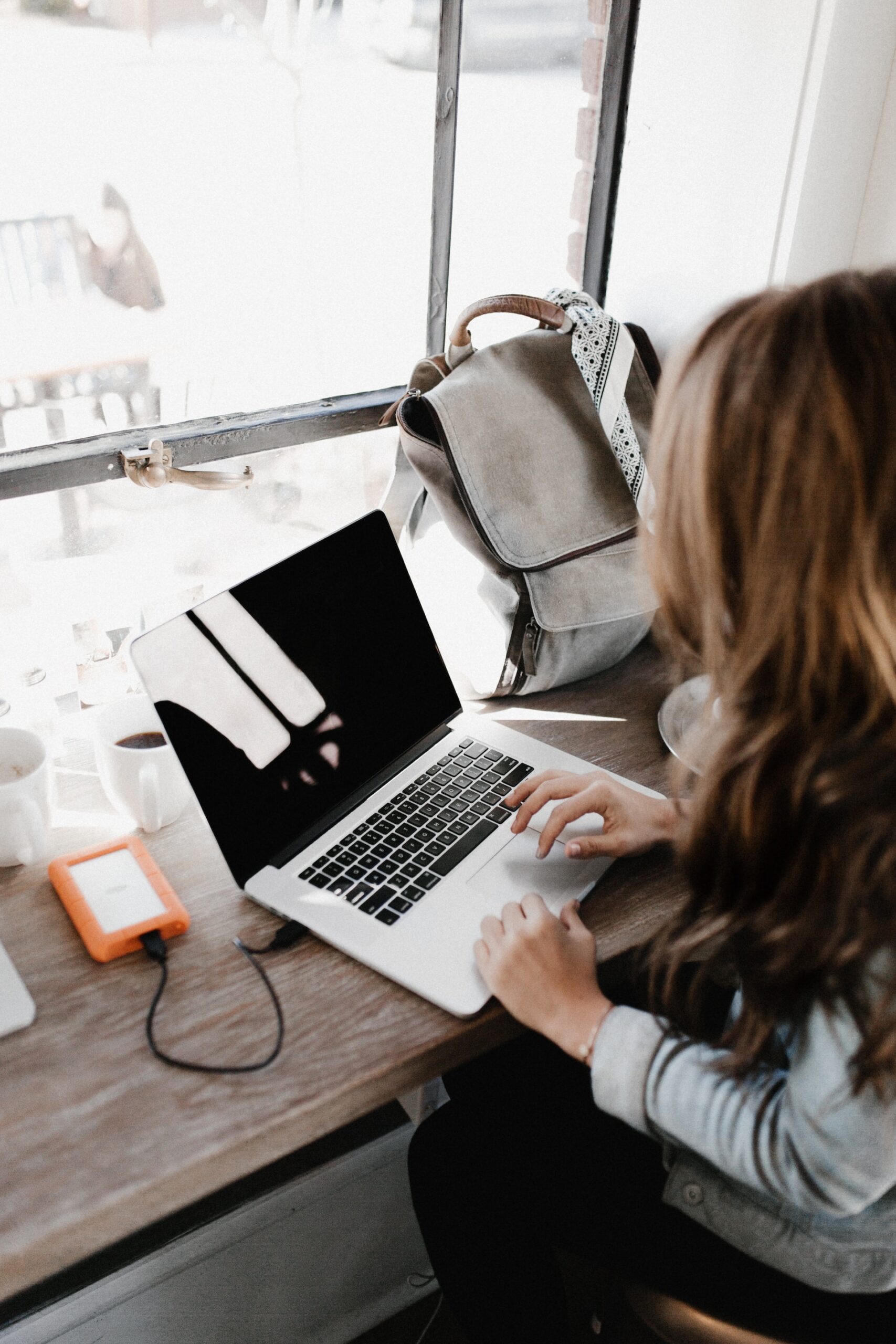 A woman working at a laptop in front of a wide window