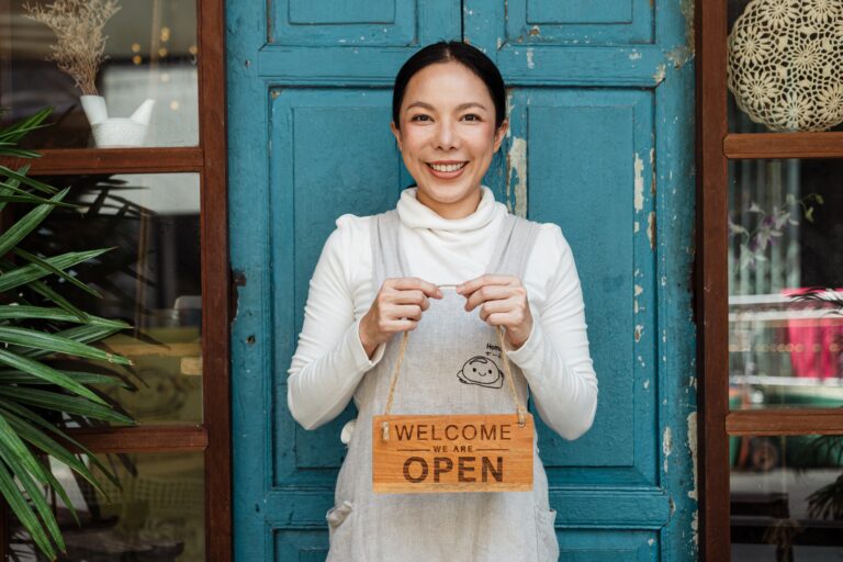 Woman standing outside of a business holding an open sign.