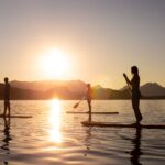 Three people standing on paddleboards in a lake during sunset.