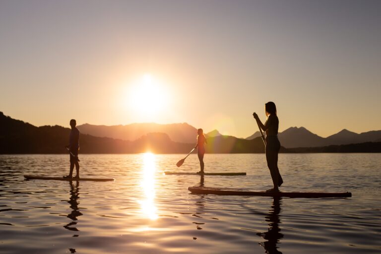 Three people standing on paddleboards in a lake during sunset.