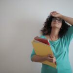 Woman holding binders filled with papers in her arm while looking stressed.