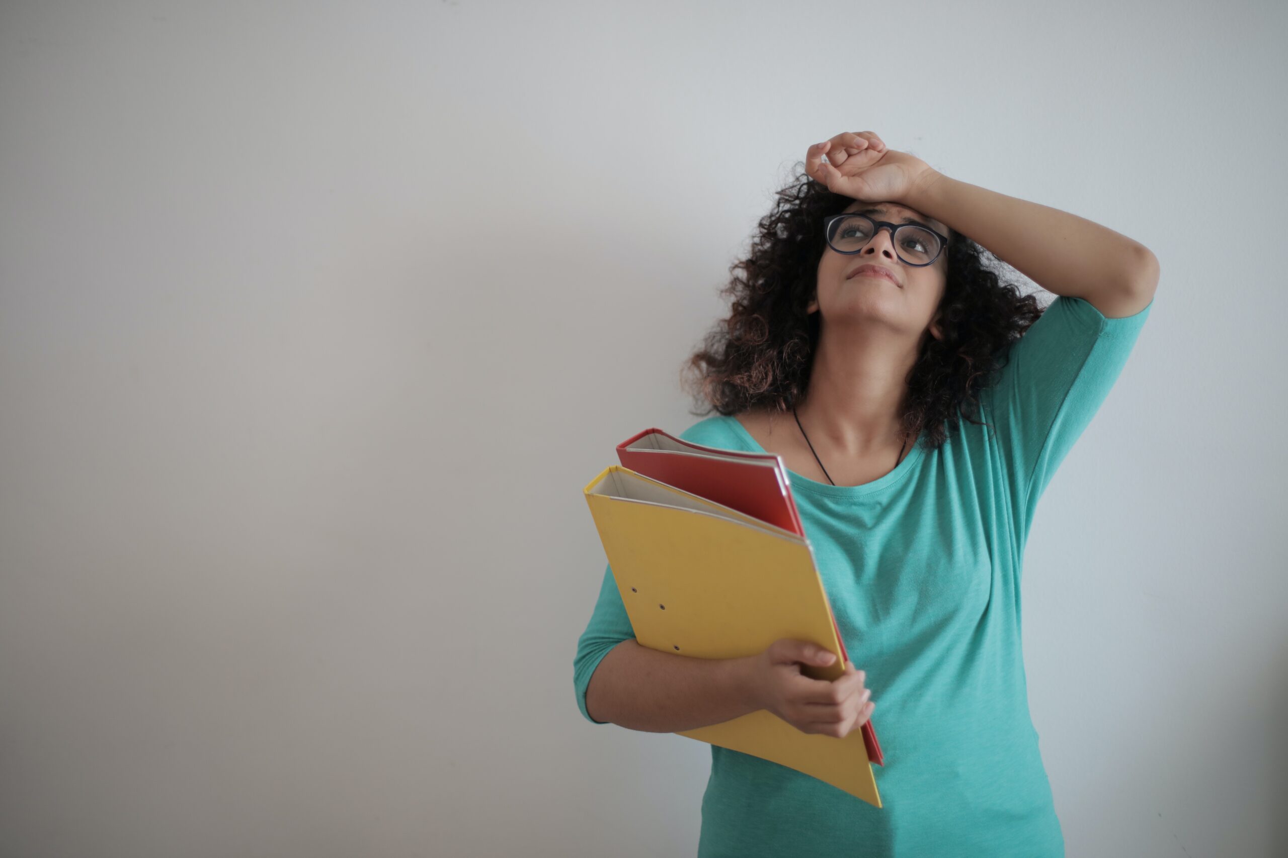 Woman holding binders filled with papers in her arm while looking stressed.