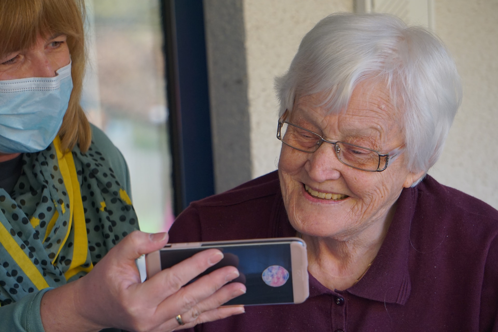 An elderly woman looking at a picture on another woman's phone