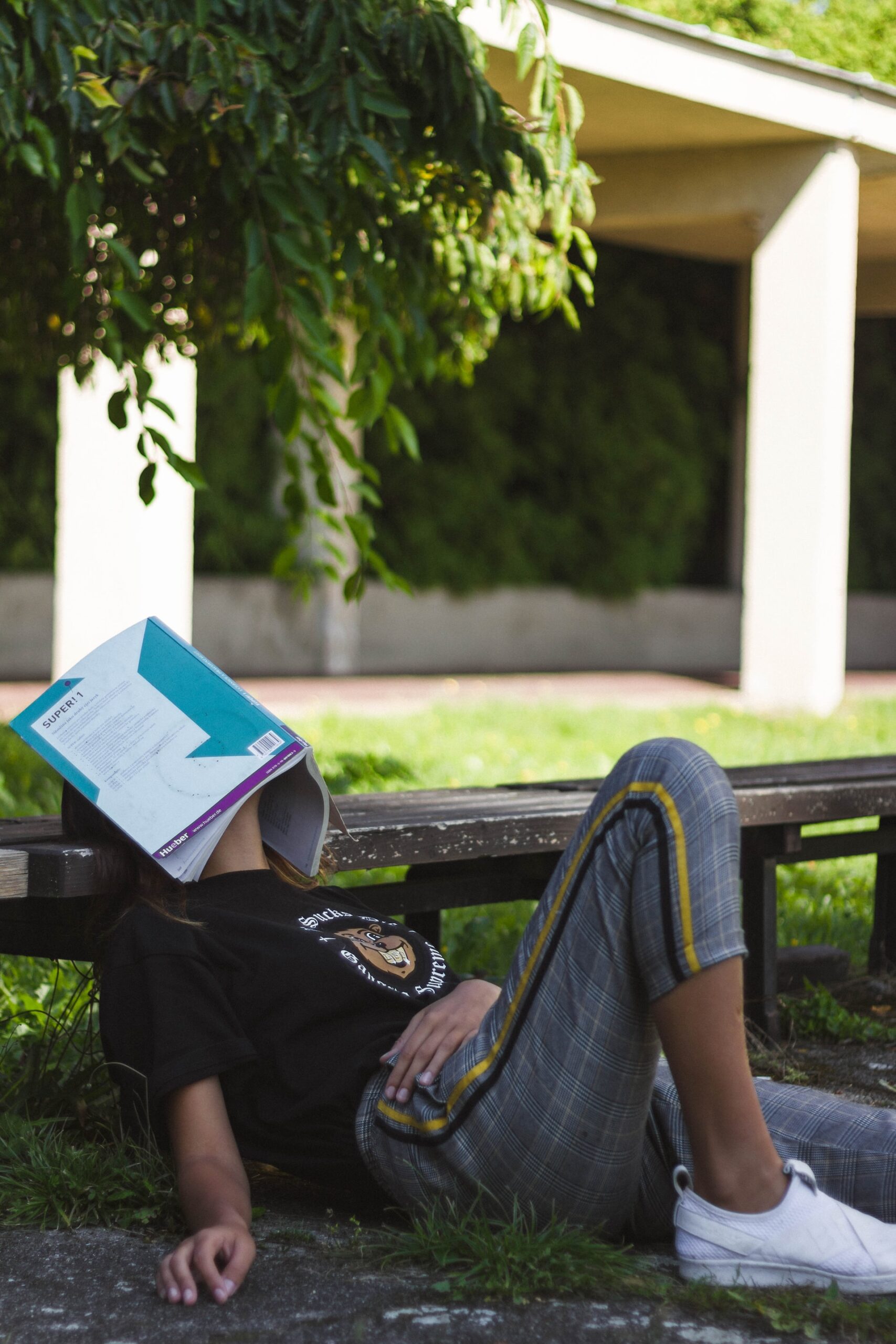 A student sitting on the ground with a textbook on their face, dozing off.