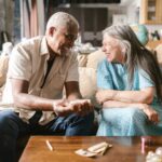 Older couple sitting together on a couch while smoking and smiling at each other.