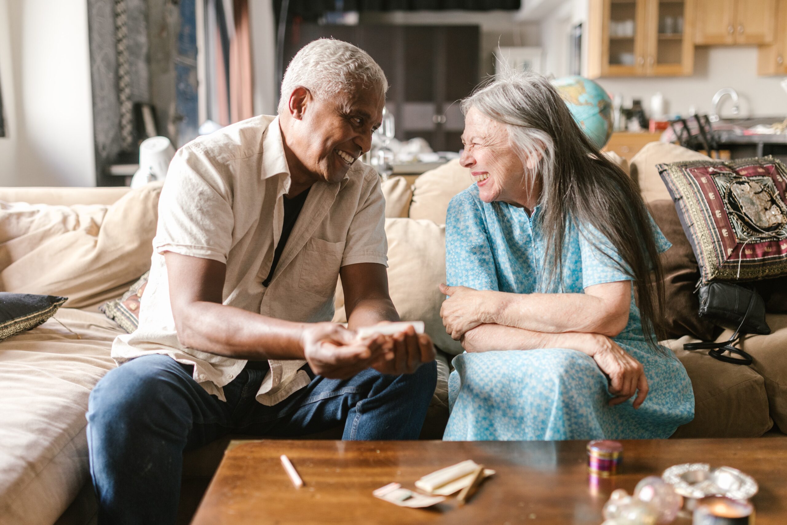 Older couple sitting together on a couch while smoking and smiling at each other.