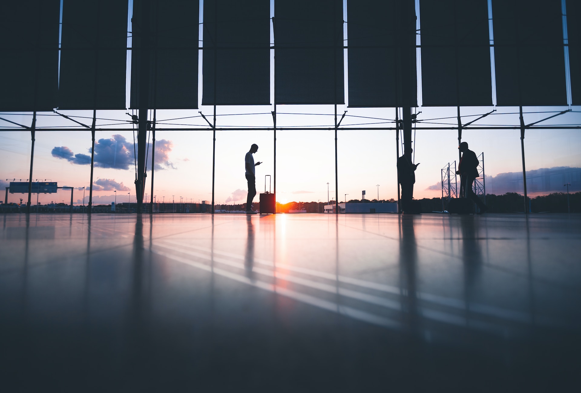 Silhouetted people lit by a sunset in an airport hallway.