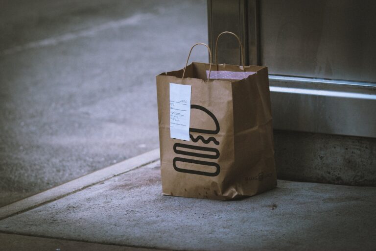 A delivery of food in a paper bag left on a front doorstep.