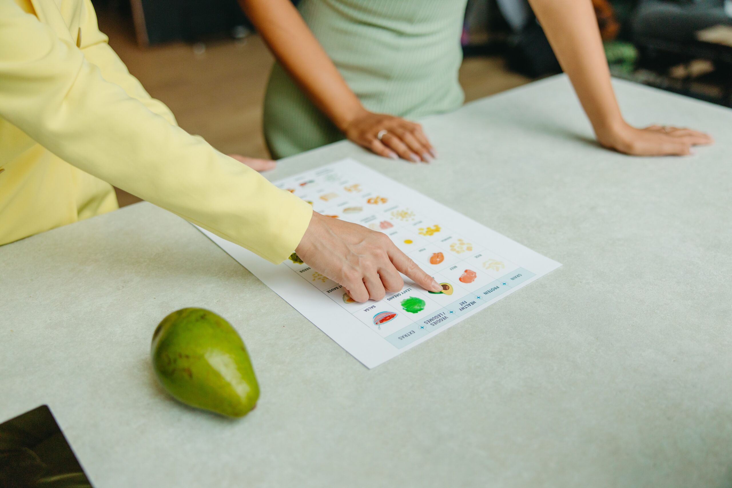 Person pointing at a sheet of paper on a table that shows different types of foods.