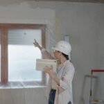 A woman in a hard hat on a construction site consulting a smart tablet and pointing.