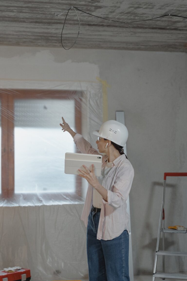 A woman in a hard hat on a construction site consulting a smart tablet and pointing.