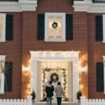 A man and a woman walking into a festively decorated home with snow on the ground.