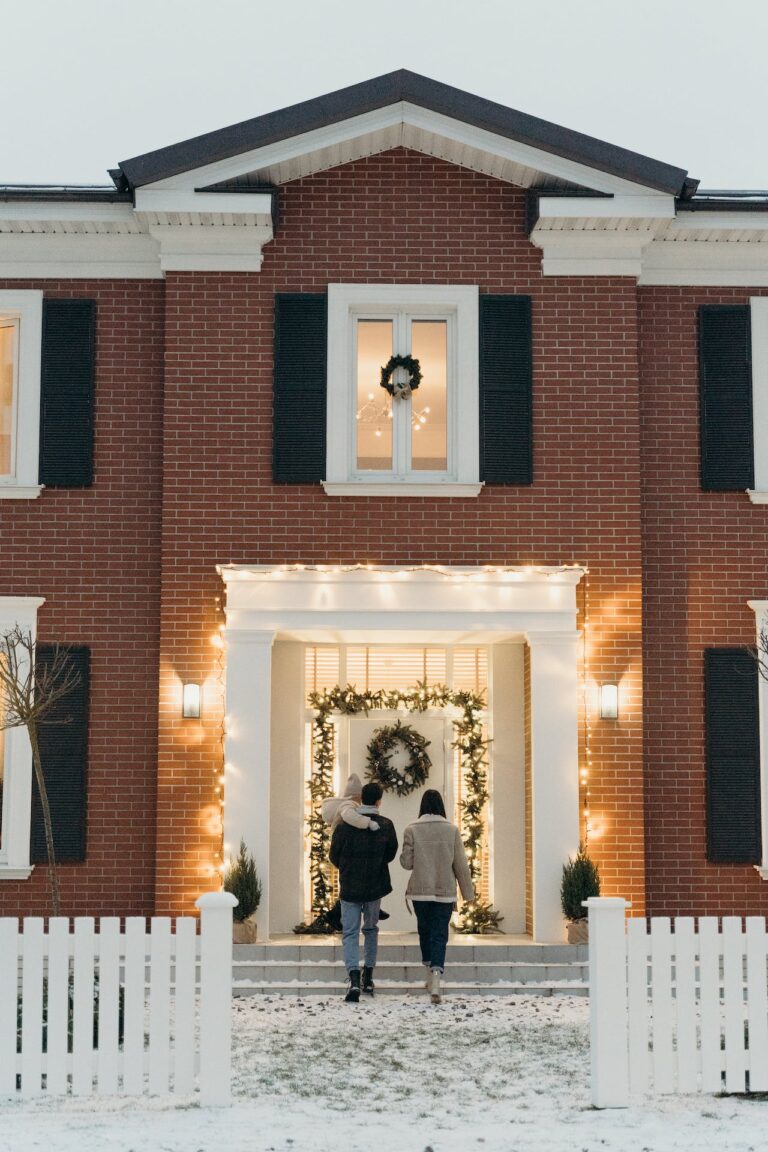 A man and a woman walking into a festively decorated home with snow on the ground.