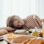 A young girl looking despondent at a table set with lots of food.